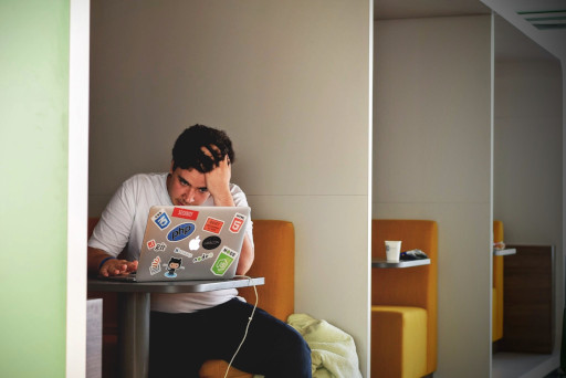 Man sitting on a bench with a laptop and his head in his hand